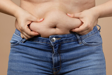 Caucasian fat woman touching overweighted belly with hands wearing blue jeans. Visceral fat. Body...
