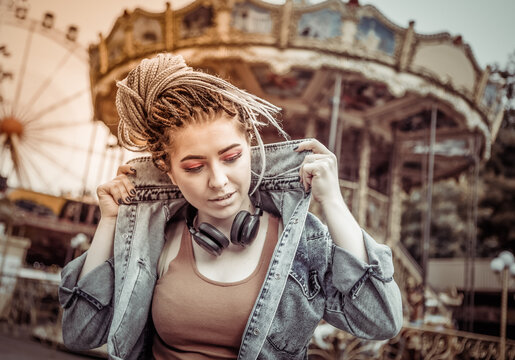 lifestyle portrait of extraordinary hipster woman with african braids dressed in denim jacket in an amusement park