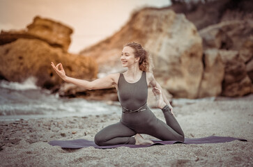 Fototapeta na wymiar Pretty young healthy yogi woman practicing hatha yoga or asana posture at sea coast with stones. Healthy lifestyle.
