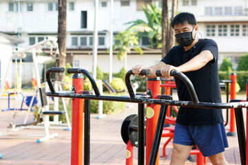 Asian man wears black face mask is exercising on exercise machine at the outdoor park. Concept: Healthcare, self protecting from coronavirus or Covid-19. Self awareness when using public park.        