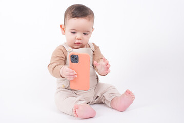 Adorable caucasian baby boy sitting on the floor over white studio background holding telephone and watching streaming video cartoons. 