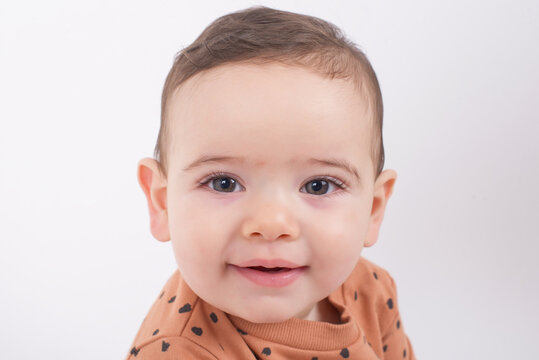 Close up portrait of an adorable sweet baby sitting over white studio background wearing animal print sweater and smiling to the camera. Childhood, innocence and happiness concept. 