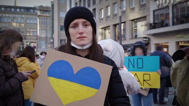 A pretty young Ukrainian woman holds a cardboard with the Ukrainian flag in the shape of a heart. She protests crying against the war in Ukraine. (1)