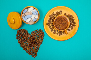 A cup of coffee around a heart made of coffee beans and colored almond candy on the side. top view composition