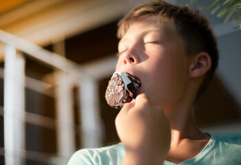 Boy teenager eats chocolate popsicle. Closed eyes in pleasure. Ice cream in the heat.