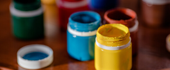 Jars of colorful paint for drawing are on desk. Bright gouache or watercolor paint. Background.