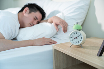 Asian attractive young man sleep while alarm clock ringing in morning. 