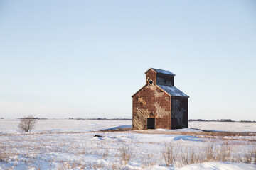 A small abandoned vintage wooden grain elevator in a lonely prairie winter landscape