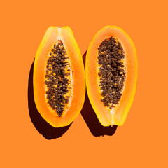two ripe papaya halves with seeds on orange background