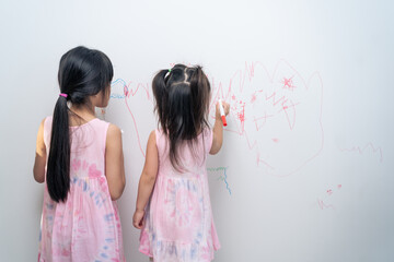 Asian young sibling kid girl enjoy paint on white wall in living room. 