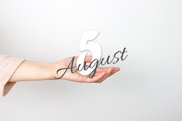 August 5th. Day 5 of month, Calendar date. Calendar Date floating over female hand on grey background. Summer month, day of the year concept.