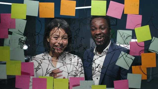 Happy African-American colleagues look at glassboard with notes and gesture high-five