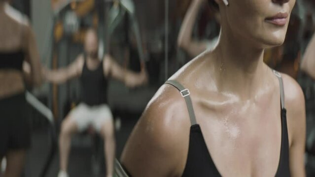 A young sweating woman runing on the running track at the gym. Reflection in the mirror of a man working out. Close up on a girl chest. Sportwear. Sport. Workout. Muscles