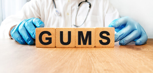 A young male doctor in blue medical gloves holds cubes with the inscription GUMS Health and...