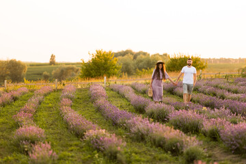 Stylish young adult couple walking at lavender field, having a romantic date. Handsome man hold a hand of beautiful woman, enjoy moments together, meeting the sunset, spend weekends outdoors concept
