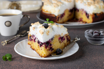 Homemade pie with black currant covered sweet meringue on plate and cup of coffee on brown background