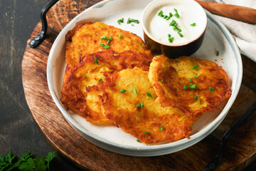 Potato pancakes. Fried homemade potato pancakes or latkes with cream and green onions in rustic plate on old wooden black table background. Rustic style. Healthy food. Top view.