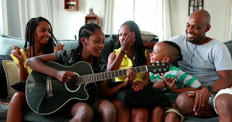 Happy African family enjoying music. Teen daughter playing guitar for parents and siblings