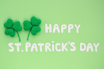 Happy St. Patrick's Day lettering with two shamrock leaves on green background. Flatlay postcard creative concept.