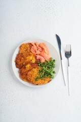 Potato pancakes. Fried homemade potato pancakes or latkes with cream, green onions, microgreens, red salmon and sauce in rustic plate on white table background. Rustic style. Healthy food. Top view.