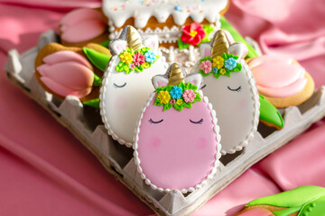 background banner greeting card for Happy Easter with colorful eggs gingerbread cookies in shape of unicorns in egg box on pink silk fabric background