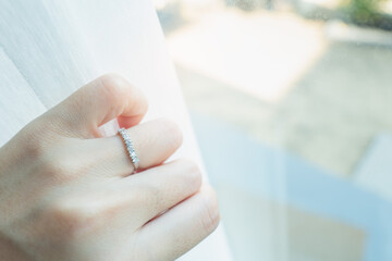 Close up of an elegant diamond ring on woman finger while touching white curtain with sunlight and...