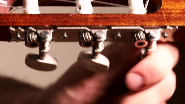 Young male guitarist hand tuning acoustic guitar. Spanish guitar tuning pegs, tuning keys.