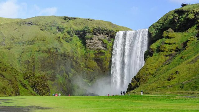 Skogafoss waterfall in Iceland Timelapse with tourists wondering around in front of the waterfall during a sunny summer day.