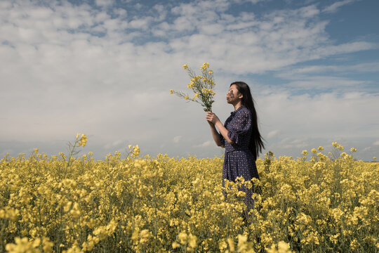 Woman in classic blue dress standing in field of yellow musterd seed flowers in spring