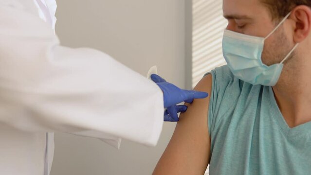 Senior nurse giving Covid-19 or flu antivirus vaccine shot to young male patient wear face mask protection from virus disease at health clinic or hospital office. Vaccination concept