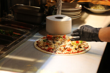 In an Italian restaurant, the pizza master prepares pizza according to customer requests. Special sauce is applied on the pizza dough and pizza ingredients are placed on it. chosen focus