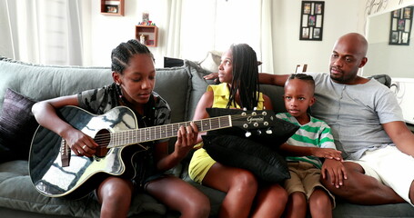 Casual black African family bonding thogether through music guitar. Daughter playing musical instrument