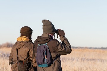Two men on their backs observing birds in nature with binoculars.