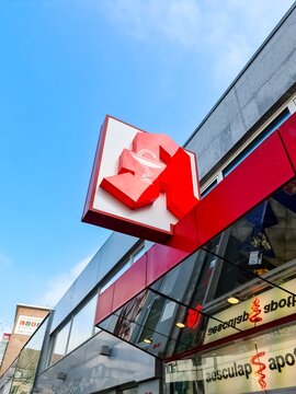 Entrance and red logo of Aesculap pharmacy in downtown shopping street.