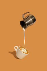 Pouring creamy milk from a stainless steel milk jug, and making late art espresso in a coffee cup...
