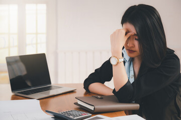 Young asian woman architect holding forehead while working on project at office desk. She is tired and tired.