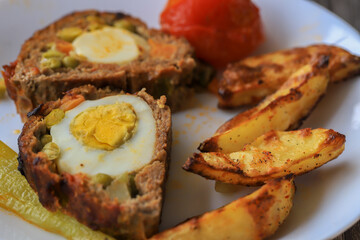 Meatloaf with egg and peas inside. Potato slices , tomatoes , peppers on the plate.