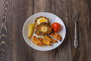 Meatloaf with egg and peas inside. Potato slices , tomatoes , peppers on the plate.