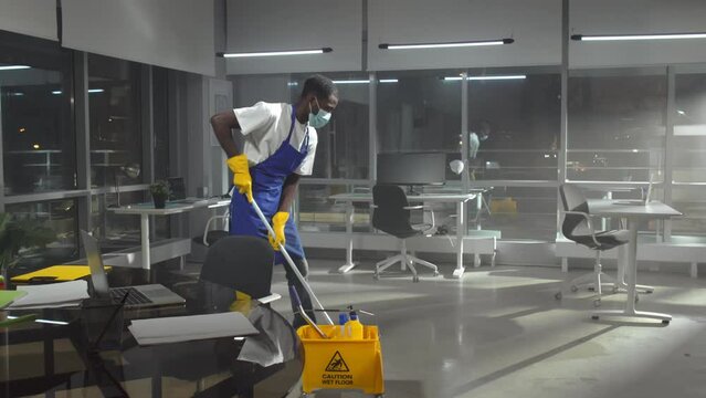 African-American janitor in facemask mop floor in empty office