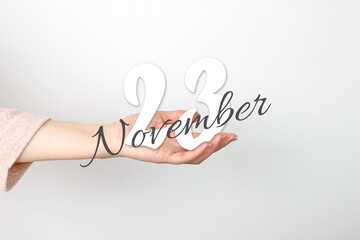 November 23rd. Day 23 of month, Calendar date. Calendar Date floating over female hand on grey background. Autumn month, day of the year concept.