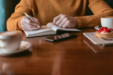 Business meeting in restaurant. Unrecognizable man writing in blank notebook, working and drinking coffee in a cafe. 