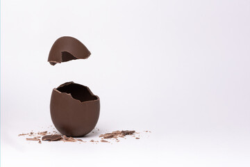 Cracked chocolate Easter egg on a light background, vertical frame, copy space. A broken milk...