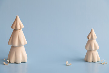 Handmade wooden carved Christmas trees with few shavings stands on blue background. Copy space for your text. Winter decoration theme.