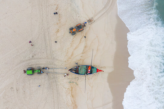 Aerial view of people along the shoreline prating the Arte Xavega, a Portuguese traditional fishing technique in Torreira, Portugal.