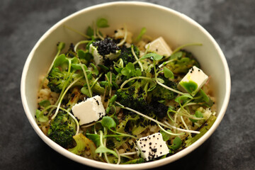Vegetarian healthy bowl with bulgur, broccoli, greens and feta cheese isolated on dark background. Healthy food delivery service and daily ration concept.