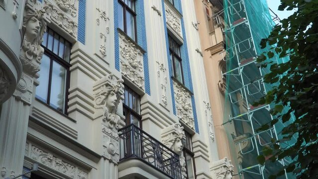 Restoration of historical buildings. A facade of the Art Nouveau building with the typical decors of this architectural style. Near it is a house with scaffolding and mesh for renovation.