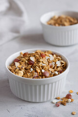 A white bowl with homemade granola on a light table. Granola with nuts and dried fruits for a healthy breakfast. Close-up. Selective focus.