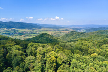 Fototapeta premium Aerial view of mountain hills covered with dense green lush woods on bright summer day.