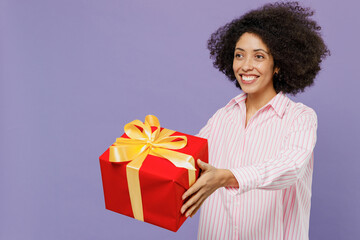 Young smiling happy fun woman of African American ethnicity 20s wearing pink striped shirt giving red present box with gift ribbon bow isolated on plain pastel light purple background studio portrait. - Powered by Adobe