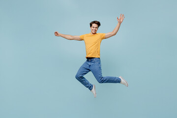 Fototapeta na wymiar Full body overjoyed fun joyful cool young man 20s wearing yellow t-shirt jumping high with outstretched hands isolated on plain pastel light blue background studio portrait. People lifestyle concept.